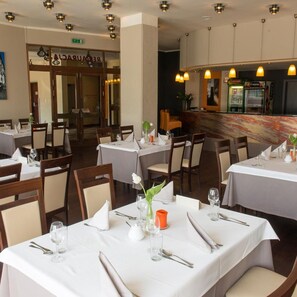 L’intérieur d’un restaurant, avec des tables dressées pour le service, un coin bar et une entrée visible donnant sur une autre pièce.