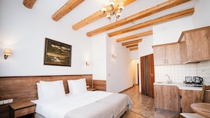 Un dormitorio con cabecera de madera, cama con ropa de cama blanca, mesita de noche, lámpara de pared y un cuadro enmarco.