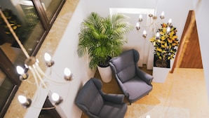 Un vestíbulo moderno con dos sillones grises, una planta en maceta grande, un candelabro decorativo y una pared de acento de madera.