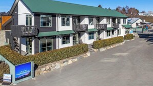 Ein mehrstöckiges Motel mit einem grünen Dach, großen Fenstern und einem Schild, das es als Lake Tekapo Village Motel kennzeichnet.