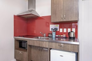 A compact kitchen with a stainless steel sink, a microwave, and a built-in oven. There is a red backsplash and wooden cabinets. - Lake Tekapo Scenic Resort (Lake Tekapo)