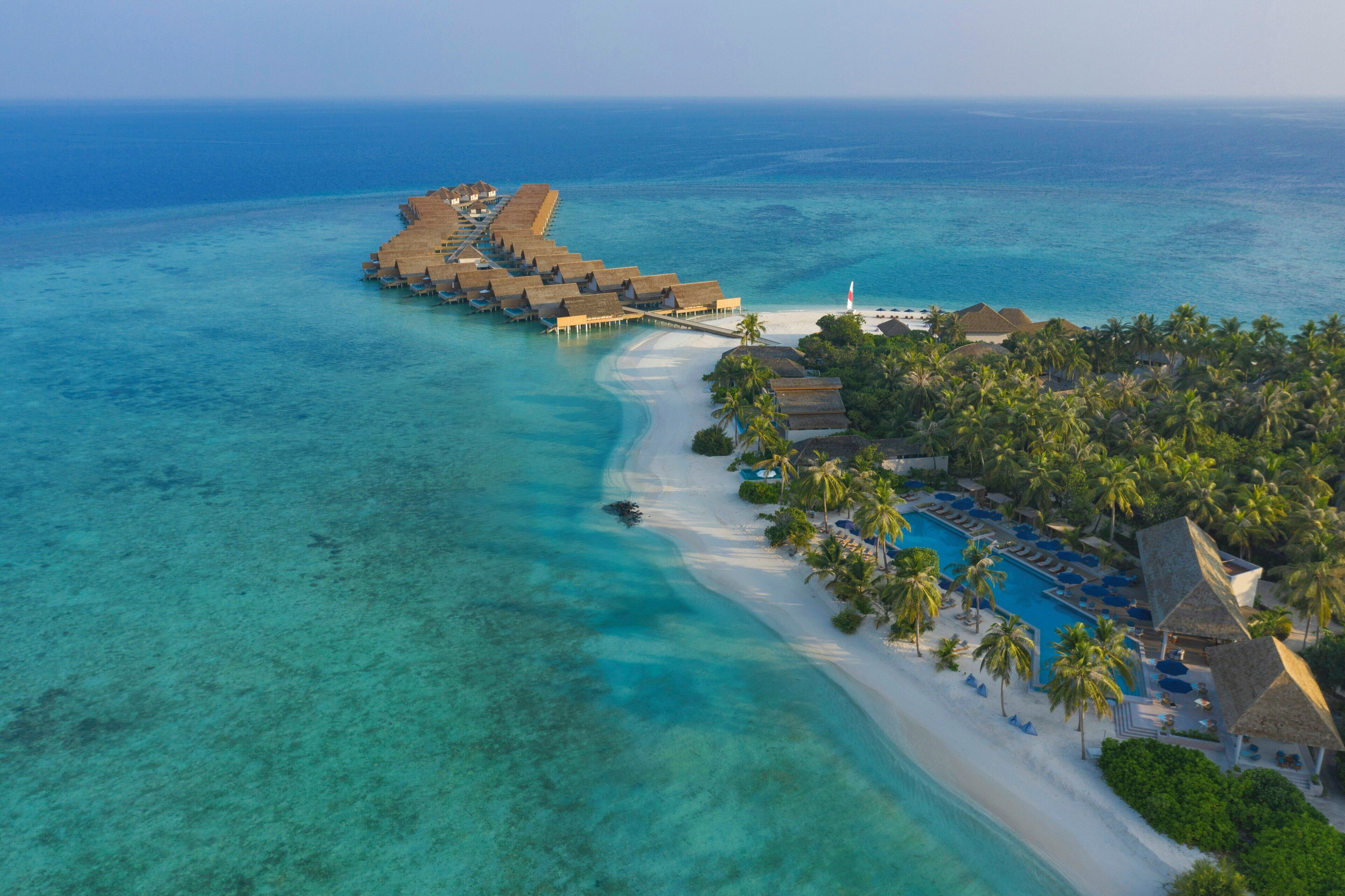 Un resort sobre el agua con varias cabañas conectadas por senderos, una playa privada y una zona de piscina.