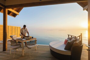A wooden deck with a dining table, chairs, and a wicker sofa overlooking a body of water. - Emerald Faarufushi Resort and Spa (Faarufushi)