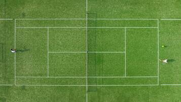 A tennis court with a net, boundary lines, and two players.