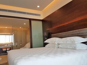 Una habitación de hotel moderna con una cama grande, cabina de ducha de vidrio y cabecero de madera.