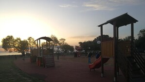A playground with a slide and climbing structures, surrounded by a red pathway and trees. - Miramare (Naousa)