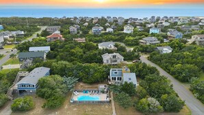 A residential area with houses, a swimming pool, and a view of the ocean at sunset. - 7221 - Wind & Waves Bungalow - Salvo Beach Bungalow w/ Pool & Hot Tub (Salvo)