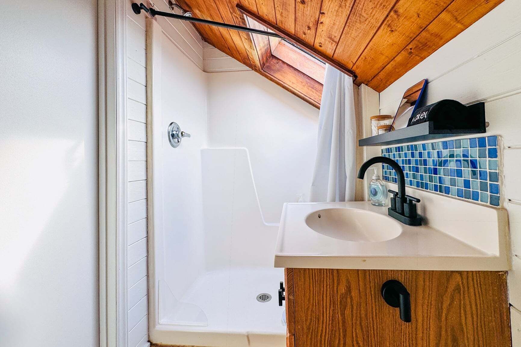 Un baño con techo de madera, bañera, ducha, lavamanos y un salpicadero de azulejos azules.