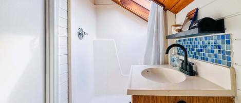 Un baño con techo de madera, bañera, ducha, lavamanos y un salpicadero de azulejos azules.