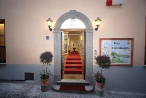 Una entrada con alfombra roja que conduce a una escalera, flanqueada por dos macetas.