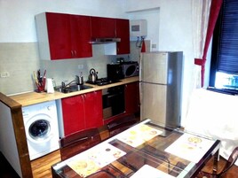 Cocina compacta con armarios rojos, lavadora, microondas y refrigerador.