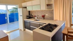 A modern kitchen with a central island, built-in appliances, and a sliding glass door leading to a balcony. - "Ap 06 Luz do Sol" 500m from Taperapuã Beach (Porto Seguro)