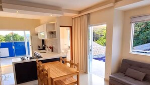 A modern kitchen with a dining area, a sofa, and a large sliding glass door leading to a balcony. - "Ap 06 Luz do Sol" 500m from Taperapuã Beach (Porto Seguro)