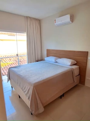 Ein Schlafzimmer mit einem Bett, einem Fenster mit Vorhängen und einer Klimaanlage an der Wand.