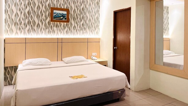 Een hotelkamer met een bed, een nachtkastje, een houten deur, een behang met patroon en een grote spiegel.