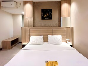 Ein Hotelzimmer mit einem großen Bett, einem Kopfteil, einem Nachttisch, einer Lampe und einer Wandklimaanlage.