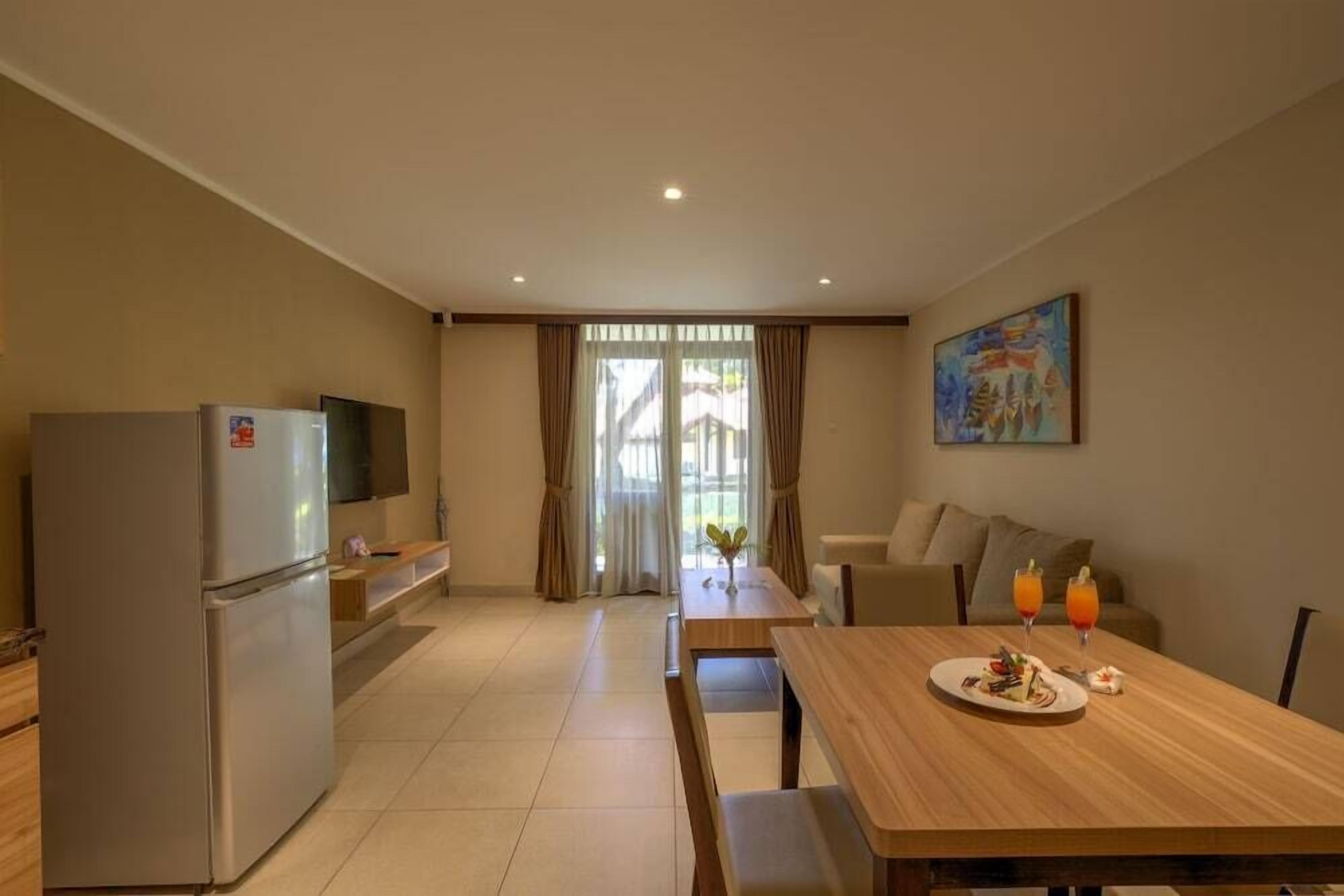 A modern kitchen with a refrigerator, a dining table with a plate of food and drinks, and a painting on the wall.