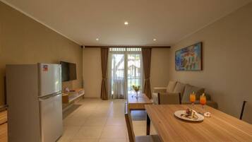 A modern kitchen with a refrigerator, a dining table with a plate of food and drinks, and a painting on the wall.