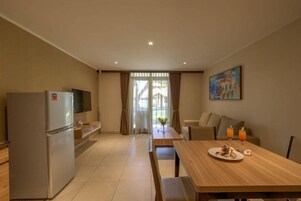 A modern kitchen with a refrigerator, a dining table with a plate of food and drinks, and a painting on the wall.