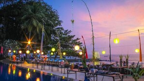 An outdoor pool area with tables and chairs, surrounded by palm trees and a sunset view. - Mambruk Anyer (Anyer)