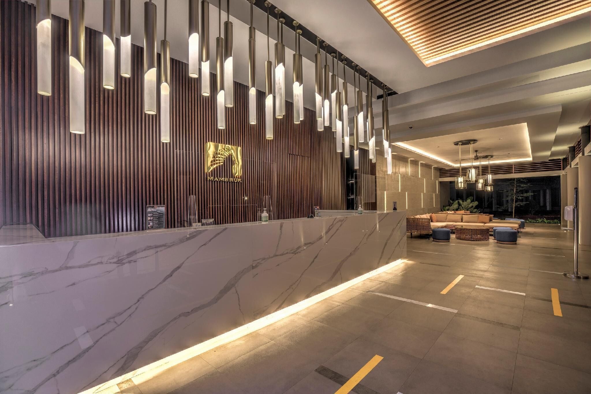 Un hall d’entrée moderne avec un comptoir de réception en marbre, des luminaires suspendus et un espace détente comprenant des canapés et des poufs.