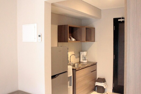 A compact kitchen with a refrigerator, coffee maker, and wooden cabinets. - Mambruk Anyer (Anyer)