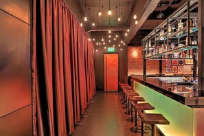 A bar area with a long counter, stools, and shelves with bottles and glasses.