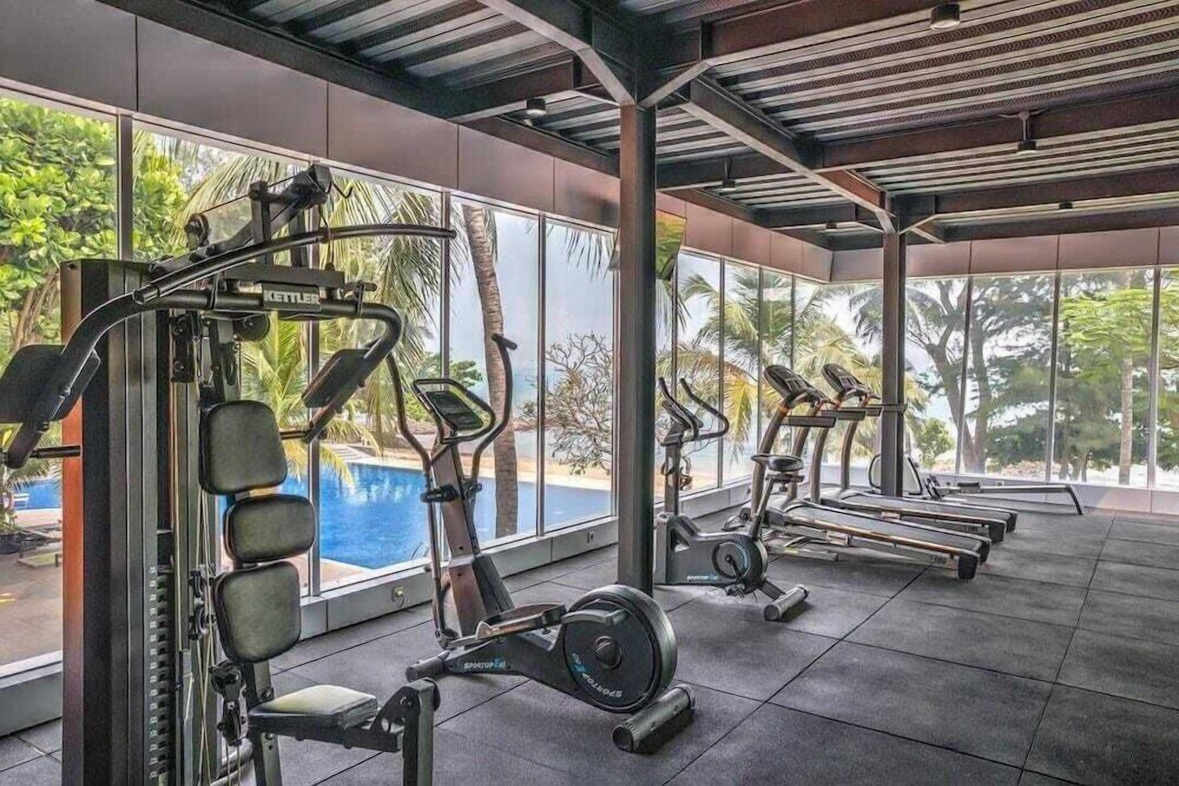 Une salle de sport équipée de machines de cardio, de matériel de musculation et offrant une vue sur une piscine.
