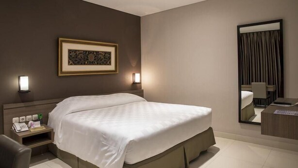A hotel room with a large bed, bedside tables, a desk, a mirror, and a framed picture on the wall. - Mambruk Anyer (Anyer)