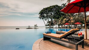 A poolside area with lounge chairs, a red umbrella, and a view of the ocean.