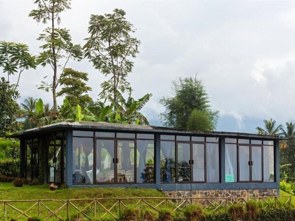 A glass-enclosed structure with a stone base, surrounded by lush greenery and tall trees. - Tea Garden Resort (Sagalaherang)