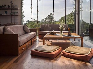 A modern living room with a sofa, a coffee table, and two poufs on a wooden floor. - Tea Garden Resort (Sagalaherang)