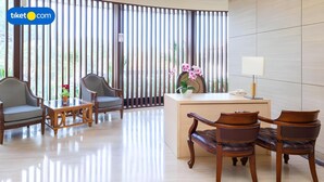 A reception area with a desk, two chairs, a small table, and a vase of flowers. - Five Premiere Hotel (Samarinda)