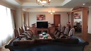 A spacious living room with a large sofa, a coffee table, and a television. There is a dining area with chairs and a table. - Five Premiere Hotel (Samarinda)