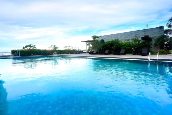 A swimming pool with lounge chairs and a modern building in the background. - Five Premiere Hotel (Samarinda)
