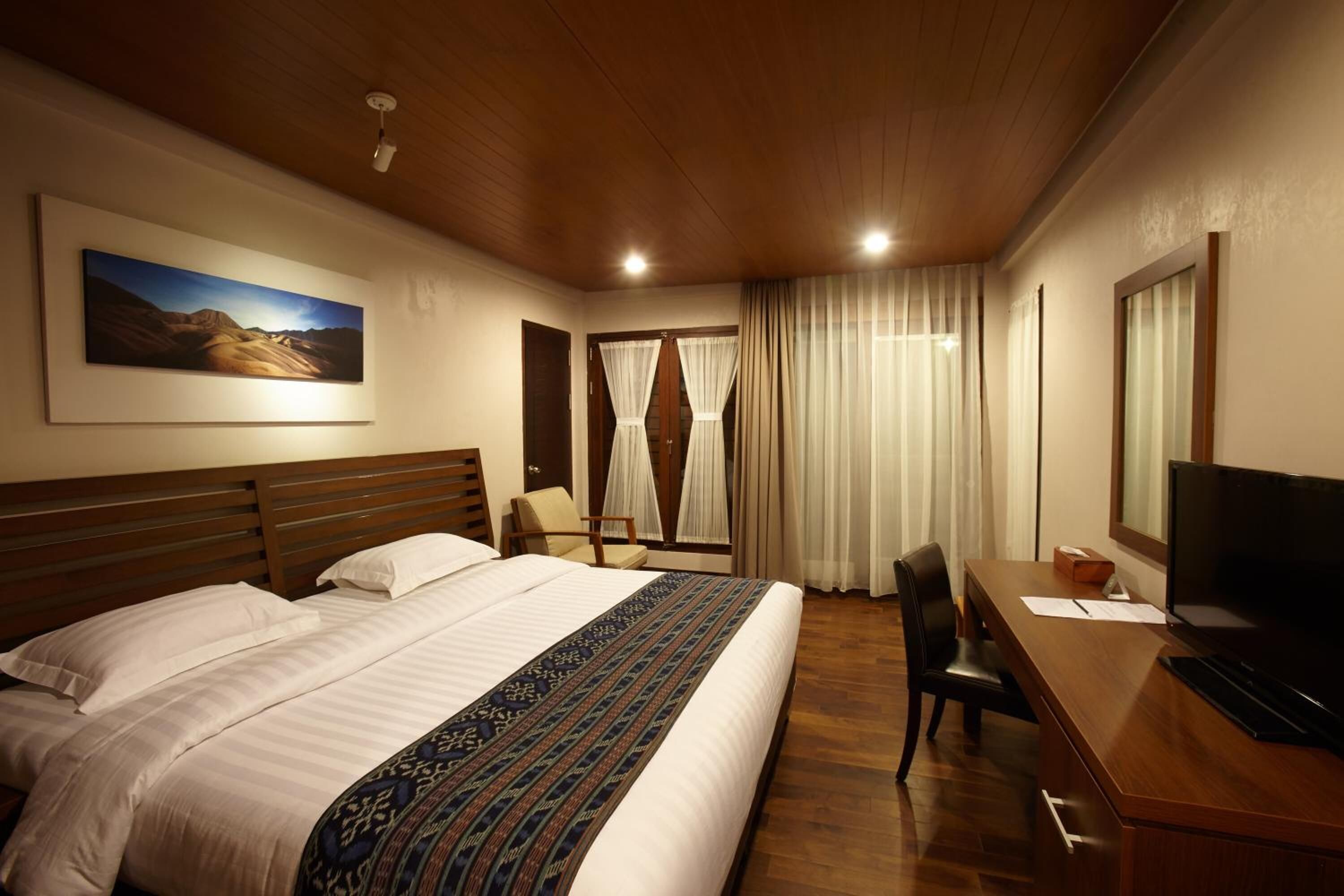 Una camera d'albergo con un letto grande, una scrivania con televisore, una sedia e una finestra con tende.