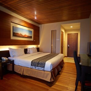 A hotel room with a wooden ceiling, a large bed with white bedding, a bedside table with a phone, a framed picture on the wall, and a door leading to another room. - Jiwa Jawa Resort Bromo (Ngadisari)