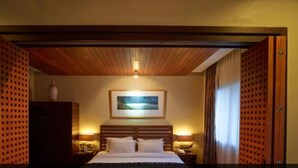 Ein Hotelzimmer mit Holzbalkendecke, einem Bett mit weißen Leinentüchern, einem gerahmten Bild an der Wand und zwei Nachttischlampen.