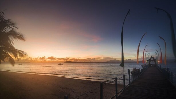 Un muelle de madera se extiende sobre aguas tranquilas al atardecer, bajo un cielo despejado.