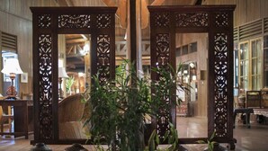 Un interior tradicional con un separador de madera con tallas intrincadas, una silla de mimbre y una planta en maceta en primer plano.