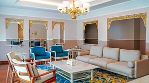 Habitación de hotel con sofá, sillas, una mesita de centro, candelabro y paredes espejadas.