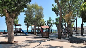 Un’area giochi con scivoli e altalene, circondata da alberi e con una vista aperta sul mare.