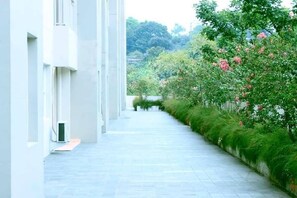A narrow, paved pathway flanked by lush greenery and white buildings. - Wood Hotel Bandung (Bandung)