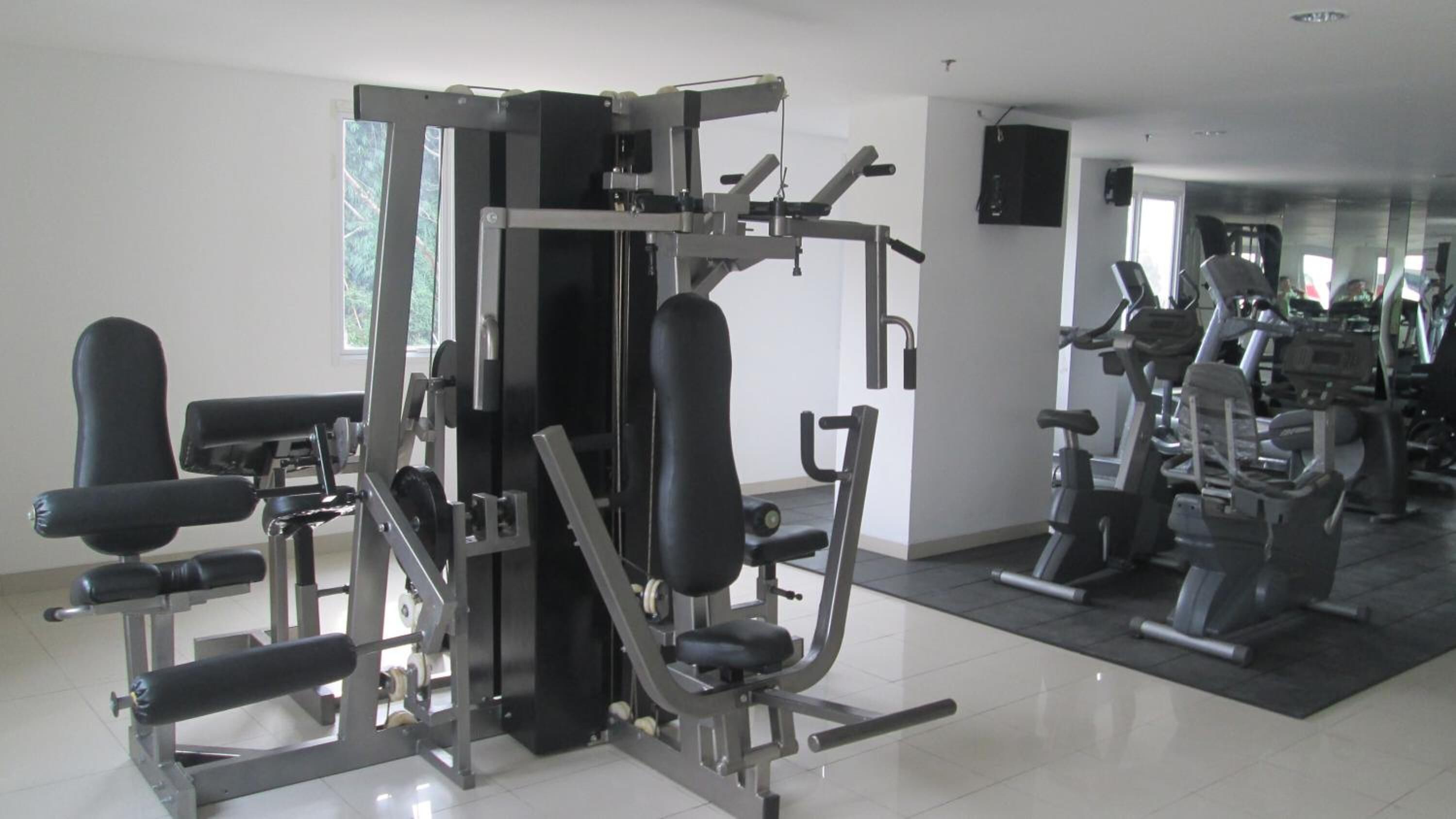 A gym with various exercise machines, a mirrored wall, and a large window.