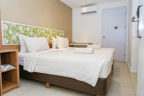 Een hotelkamer met een groot bed, een houten nachtkastje, een kleine tafel en een wandairconditioner.