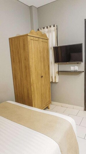 A bedroom with a bed, a wooden wardrobe, a television on a stand, and a curtain. - Triple Seven Hotel (Bandung)