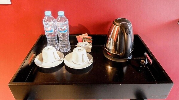 A tray with two water bottles, two white cups, a silver electric kettle, and some papers. - Triple Seven Hotel (Bandung)