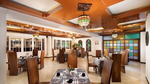 A spacious dining area with wooden tables and chairs, large windows, and a colorful wall display. - Royal Trawas Hotel & Cottages (Trawas)