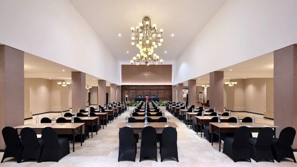 A conference room with long tables and chairs, a chandelier, and a stage at the front. - Royal Trawas Hotel & Cottages (Trawas)