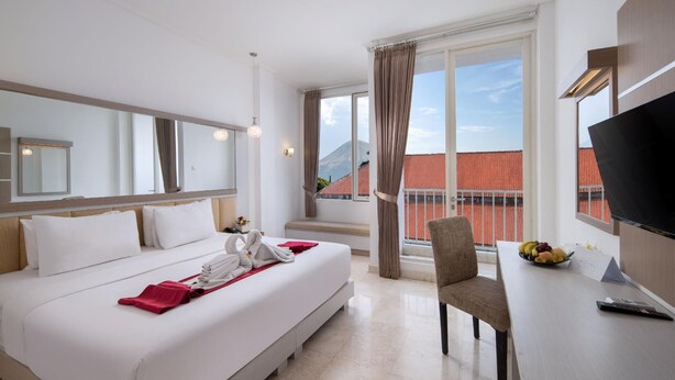 A hotel room with a bed, a desk with a bowl of fruit, a chair, and a TV. - Royal Trawas Hotel & Cottages (Trawas)